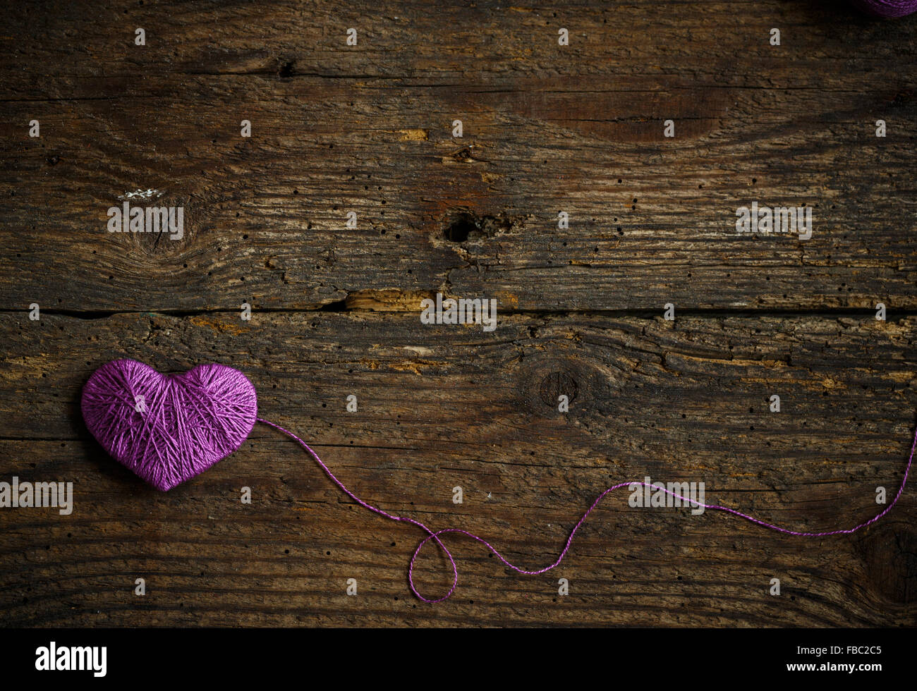 Corazón Púrpura con una bola de hilo en el antiguo fondo de madera desvencijado. Imagen del día de San Valentín Foto de stock