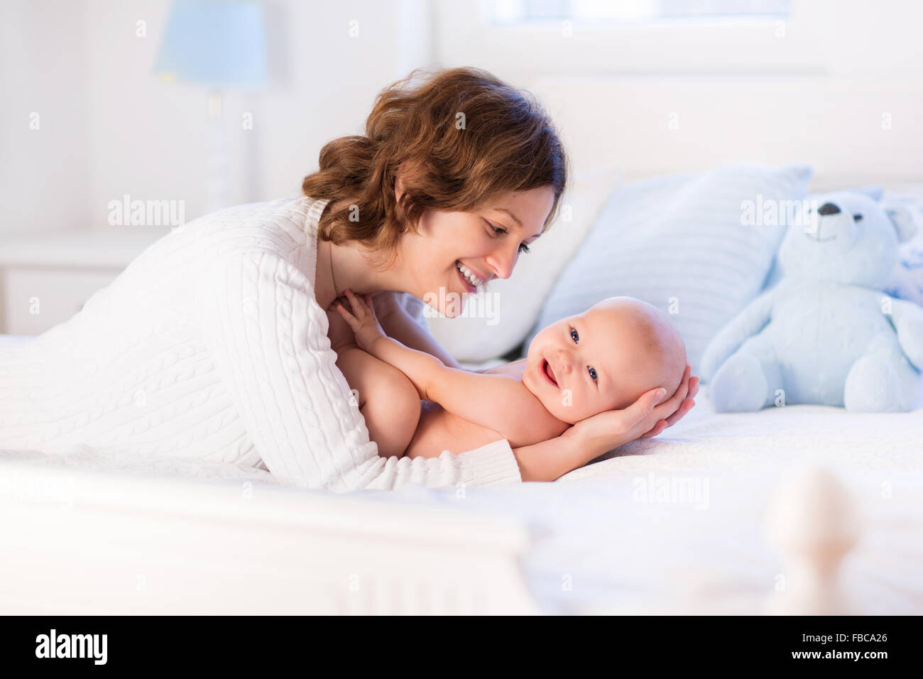 La madre y el niño en la cama blanca. La mamá y el bebé niño en pañales jugando en la soleada habitación. Padre y niño relajado en casa Foto de stock