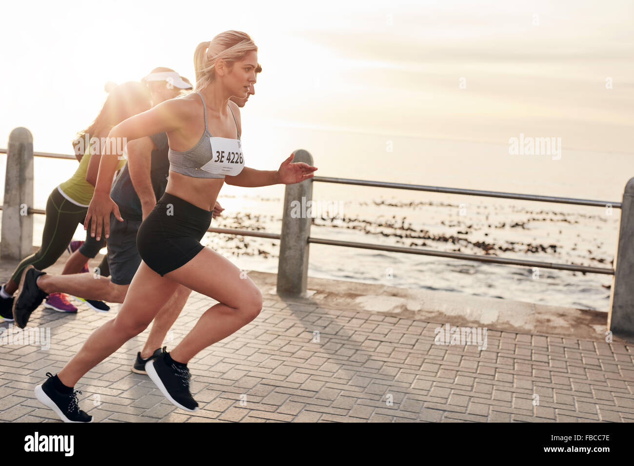 Retrato de jóvenes corriendo en el paseo marítimo. Grupo de mujeres corriendo maratón. Foto de stock