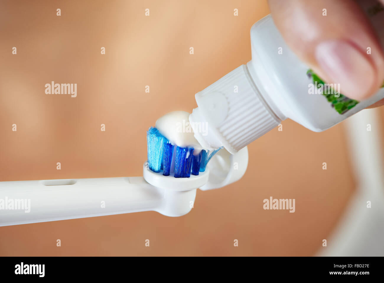 Manos apretando la pasta de dientes sobre el cepillo dental eléctrico macro closeup Foto de stock
