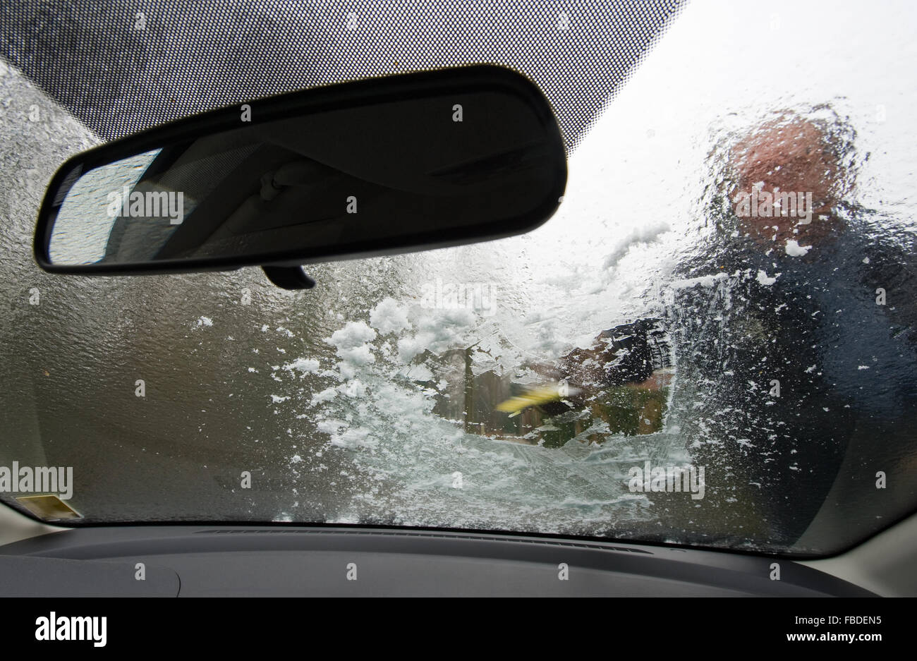 Un hombre es raspar el hielo del parabrisas de su coche Foto de stock