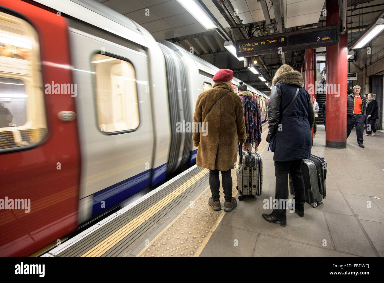 Un tubo tren llega como pasajeros de pie sobre la plataforma de una estación de metro en Londres. Foto de stock