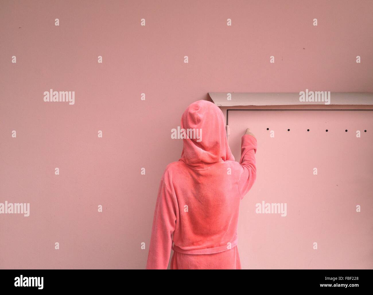 Vista trasera de una mujer en el capó contra la pared rosa Foto de stock