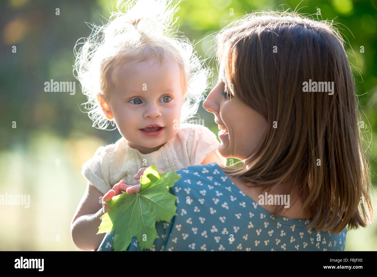 Retrato de joven feliz mamá y adorable rubia niña sonriente madre sosteniendo a su pequeña hija en brazos, hablar, jugar w Foto de stock