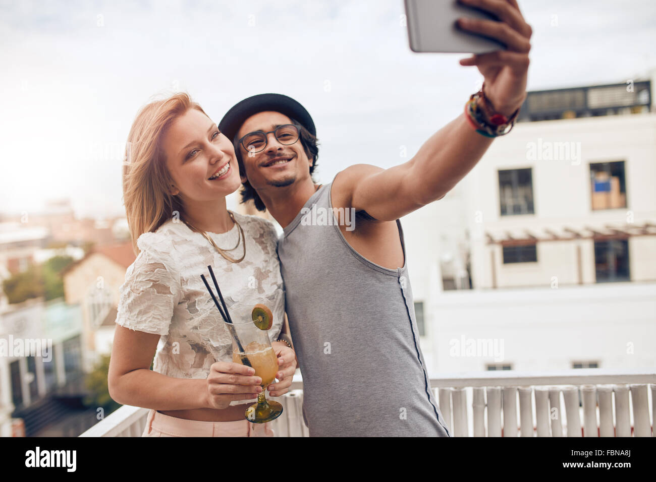 Par de amigos, una fiesta en la terraza, tomando un selfie con mujer bebiendo un cóctel. Son felices y alegres. Foto de stock