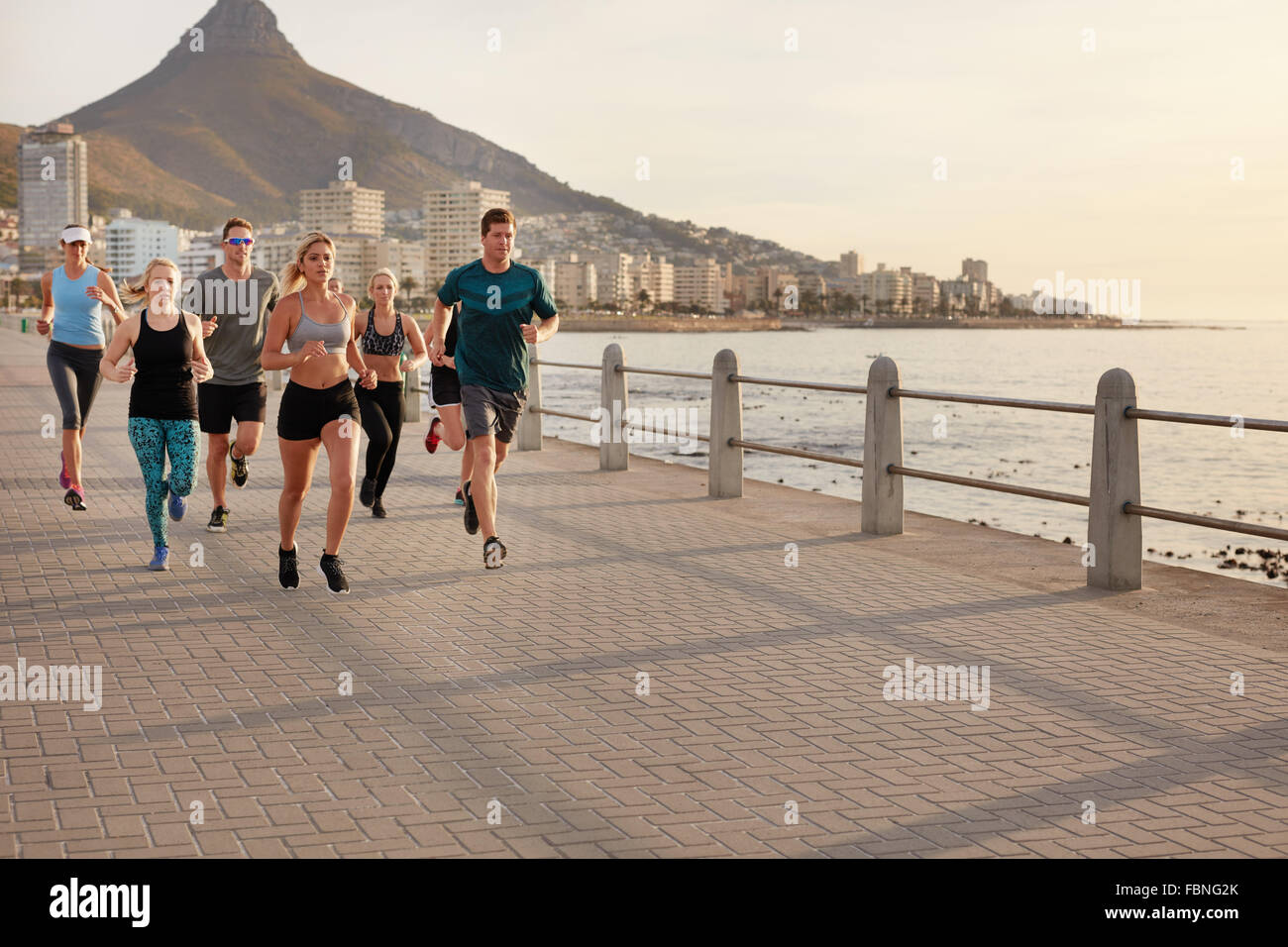 Jóvenes sanos que corre a lo largo de la orilla del mar. Ejecutando club la capacitación en grupo juntos en un paseo por el mar en la ciudad. Foto de stock