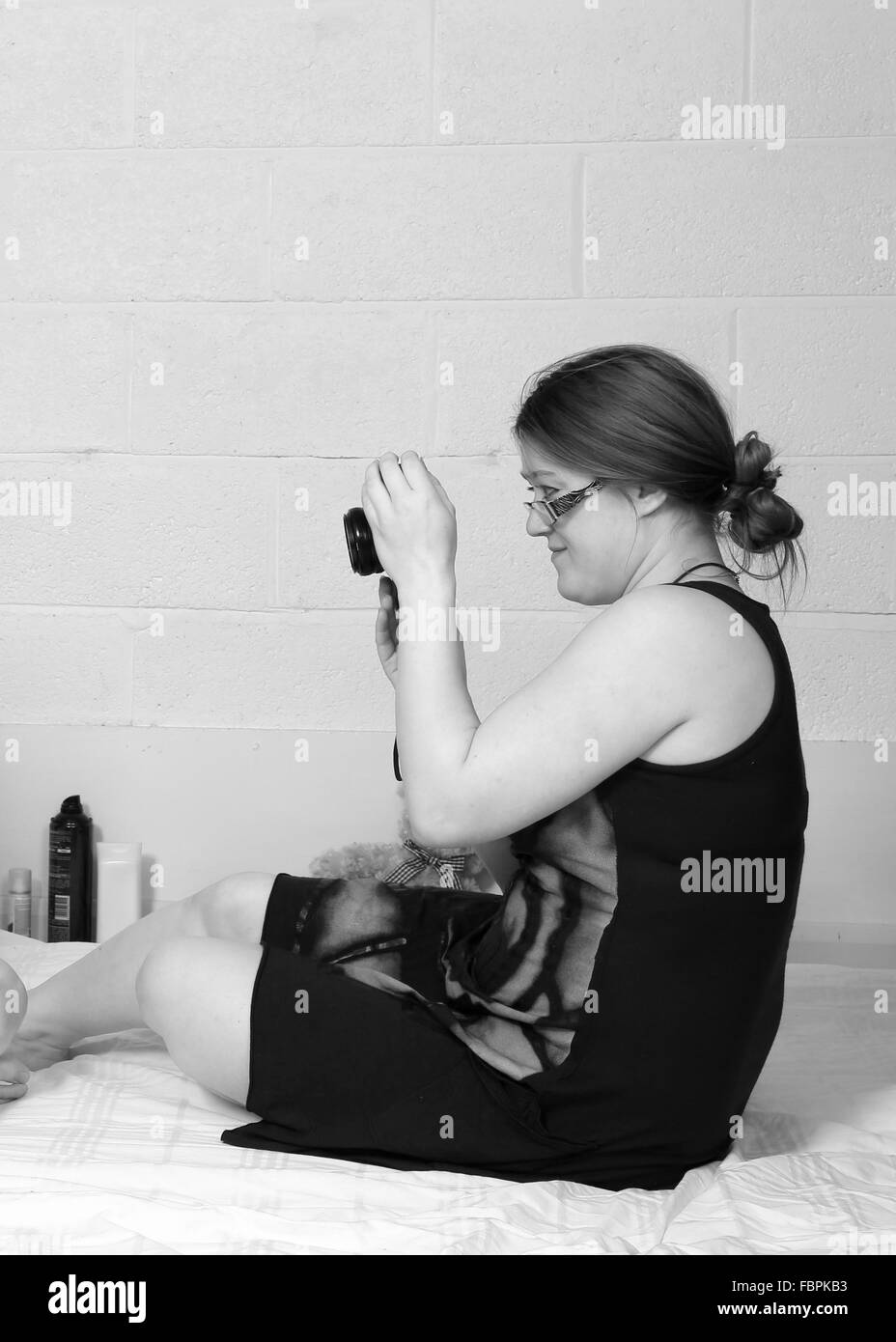 Mujer joven sentado en una cama, tomar fotos con su cámara digital, enero de 2016 Foto de stock