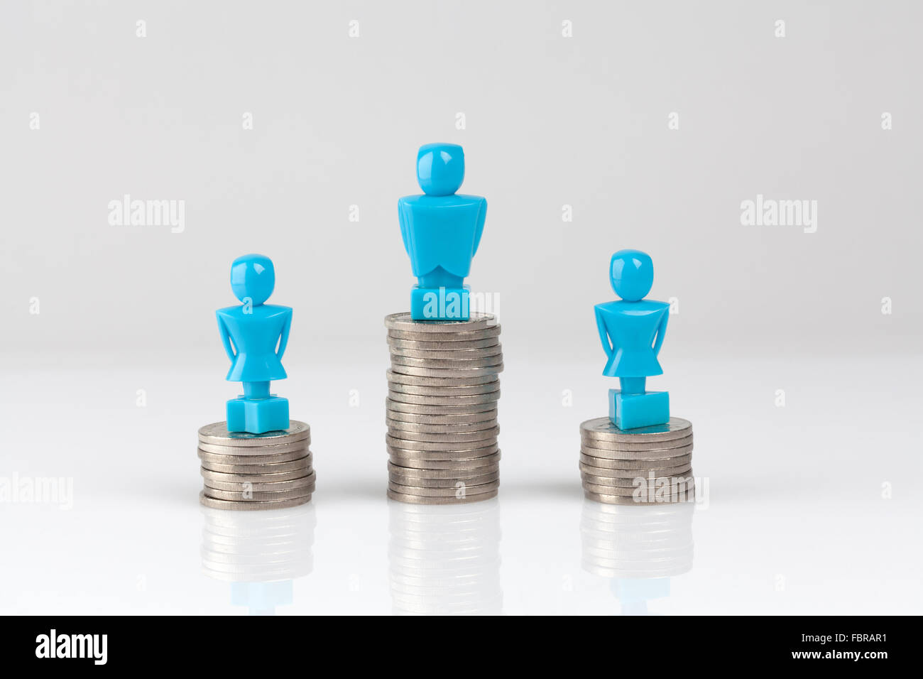 Un varón y dos figurillas femeninas, de pie en los montones de monedas. Concepto de la desigualdad de ingresos. Foto de stock