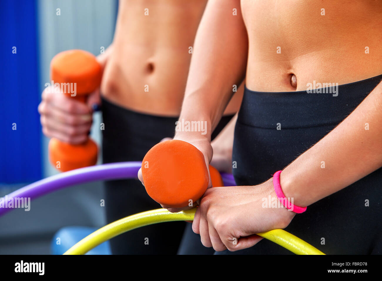 El vientre femenino desnudo con pesas en el gimnasio y el aro