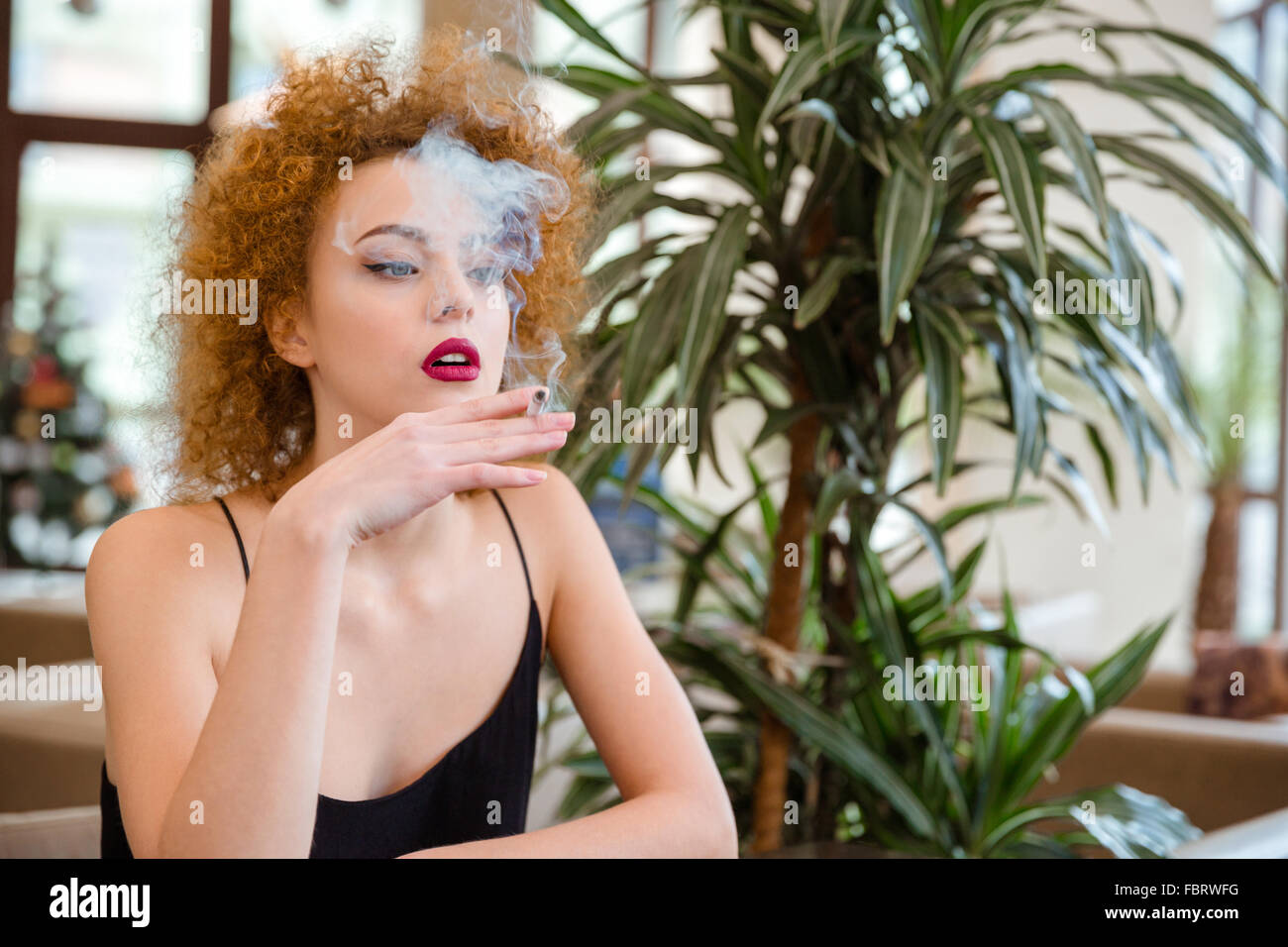 Retrato de una mujer pelirroja con el pelo rizado de fumar en restaurante Foto de stock