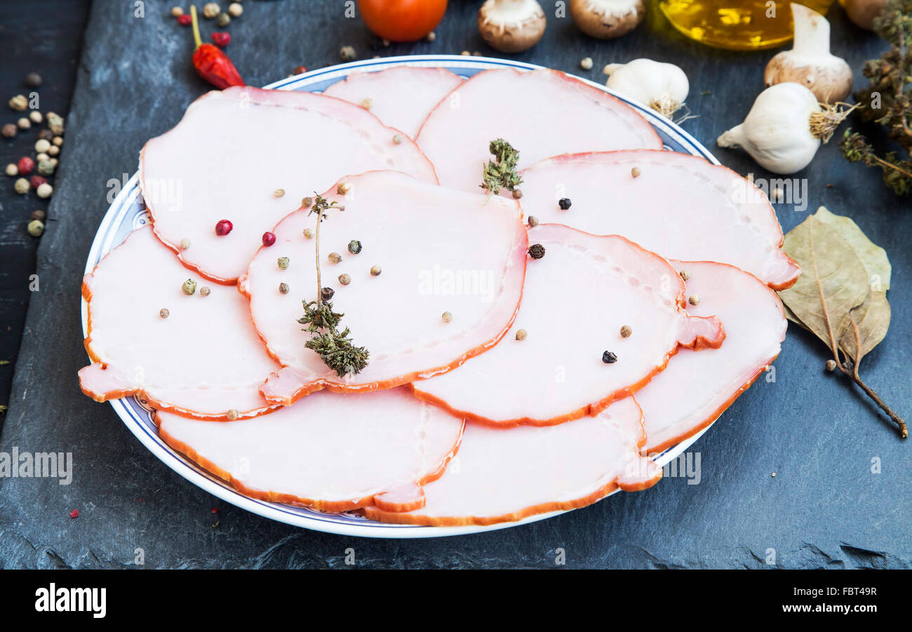 Lonchas de jamón de cerdo con especias, pimienta molida y tomillo seco sobre una placa Foto de stock