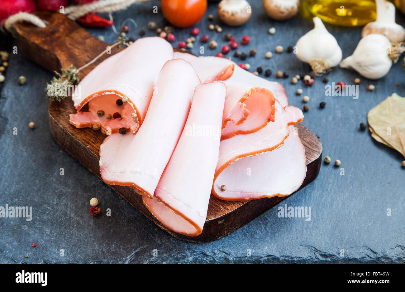 Lonchas de jamón de cerdo con especias, pimienta molida y tomillo seco sobre la tabla de cortar de madera Foto de stock