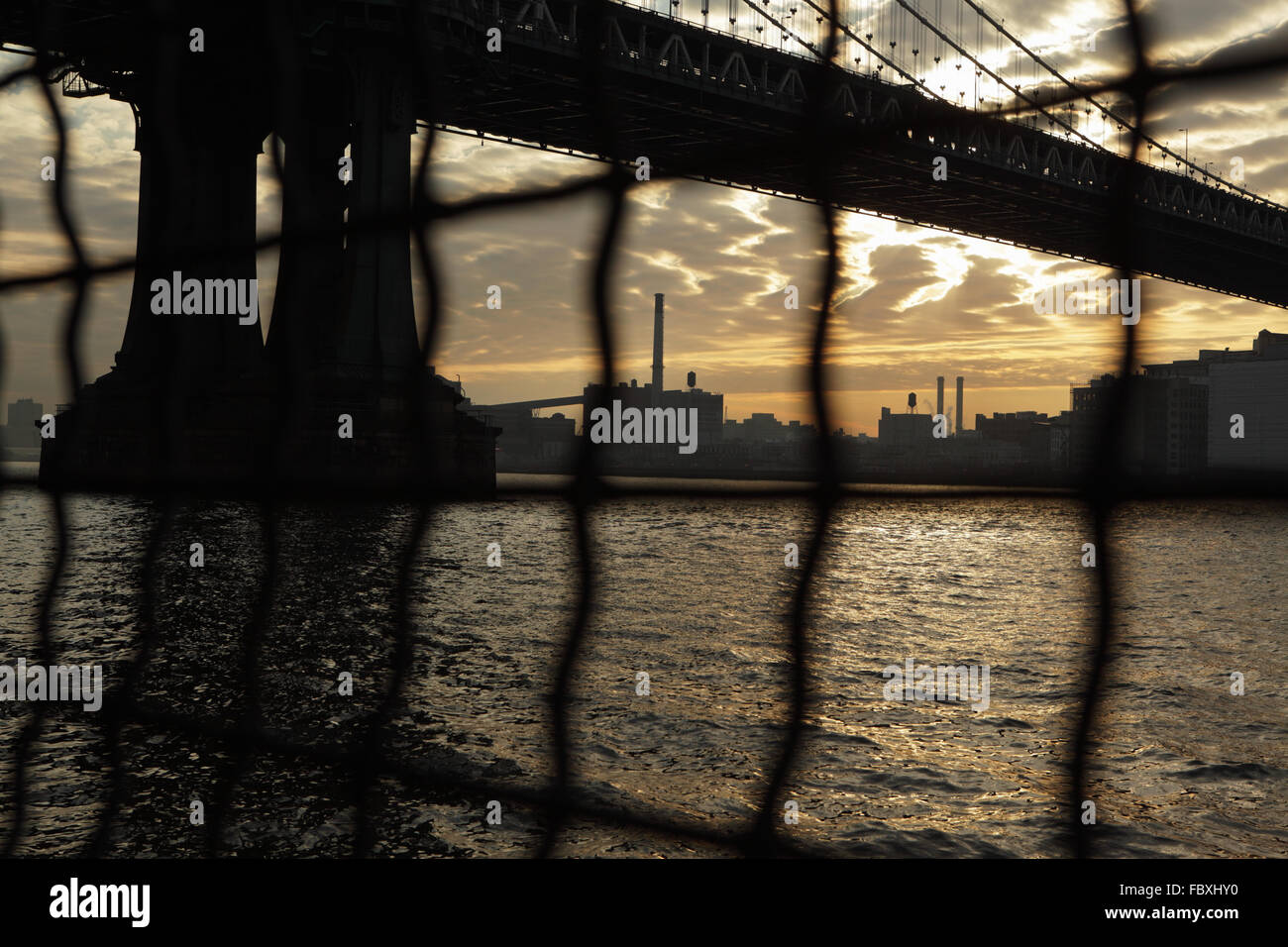 Distorsionada visión industrial de Manhattan Bridge waterfront sunrise New York City a través de una valla de alambre Foto de stock