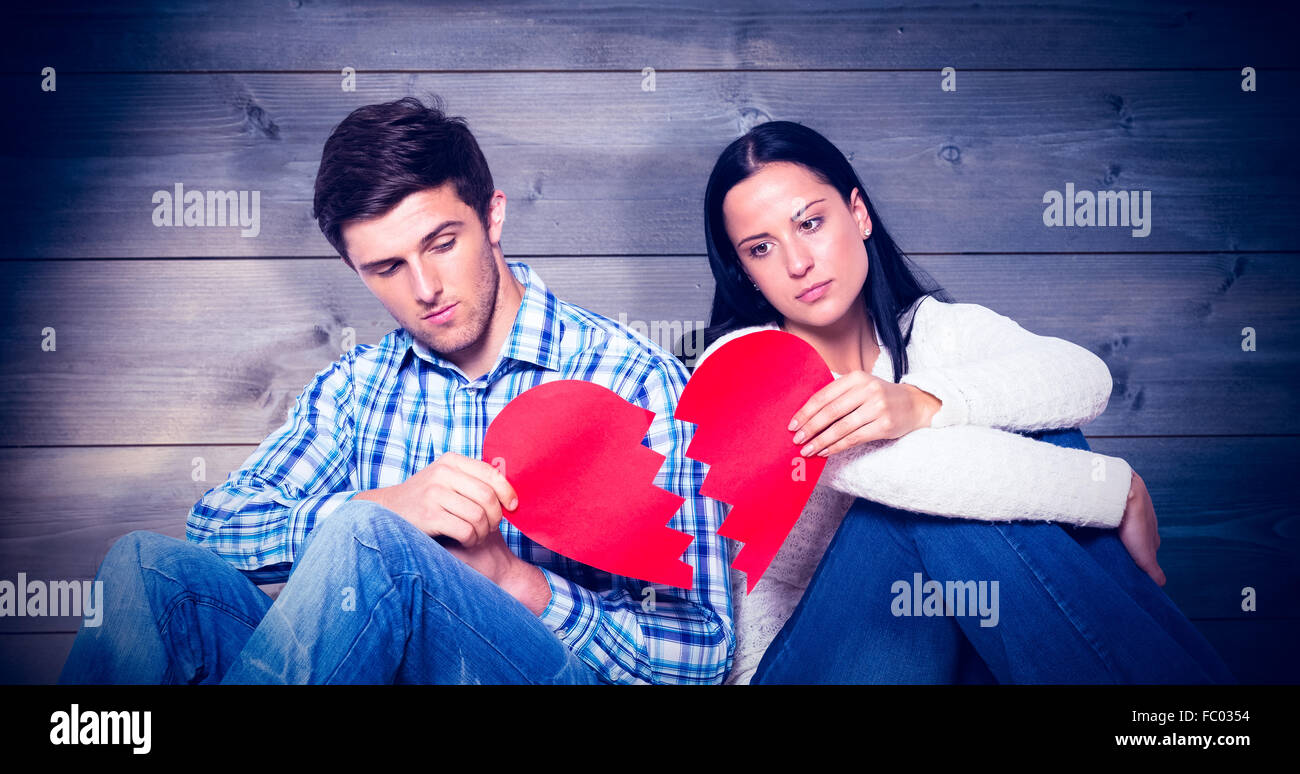 Imagen compuesta de pareja joven sentado en el suelo con el corazón roto Foto de stock