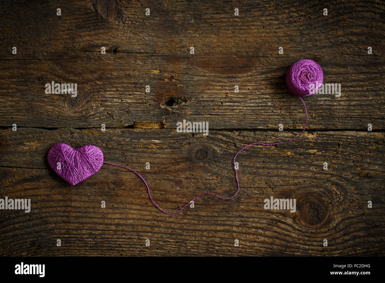 Corazón Púrpura con una bola de hilo en el antiguo fondo de madera desvencijado. Imagen del día de San Valentín Foto de stock