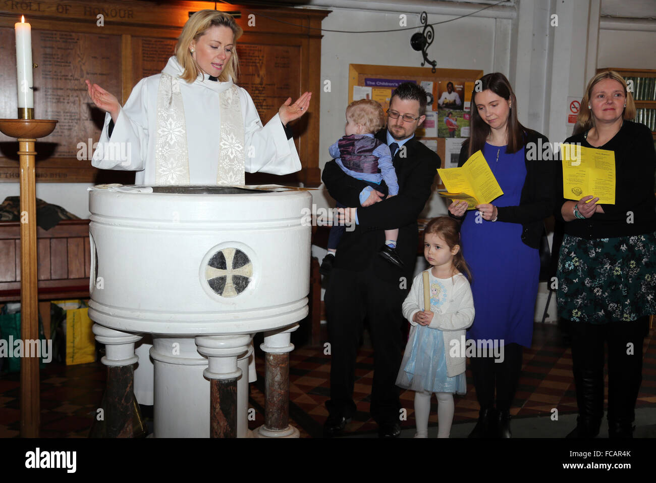 Bautizos en St Mary's Church de Caterham en la colina de Surrey, Inglaterra Mujeres sacerdote por Font con padres leyendo votos bautizo Foto de stock