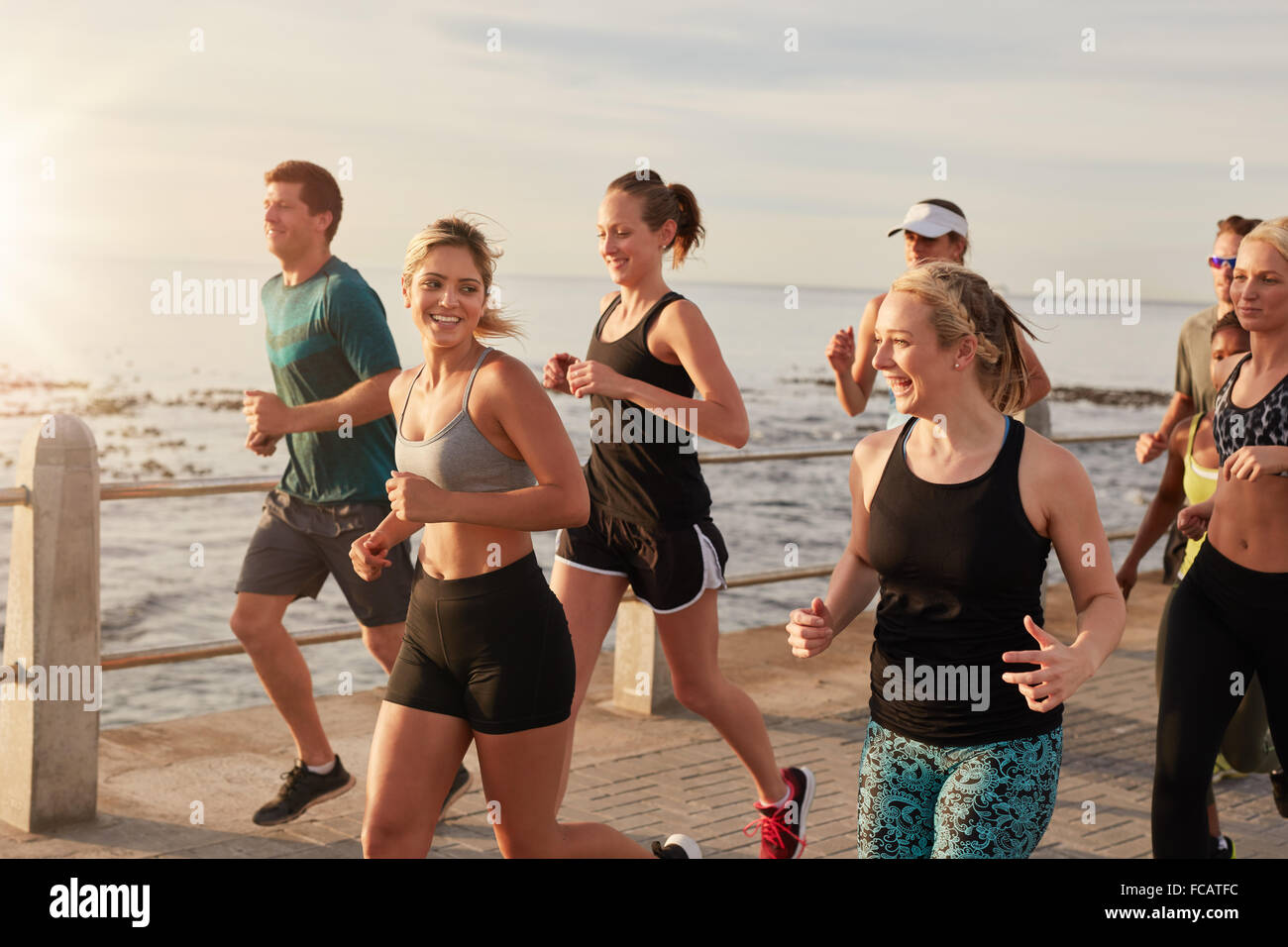 Retrato de hombres y mujeres jóvenes saludables correr juntos en el paseo marítimo. Club de funcionamiento activo la capacitación en grupo al aire libre por th Foto de stock