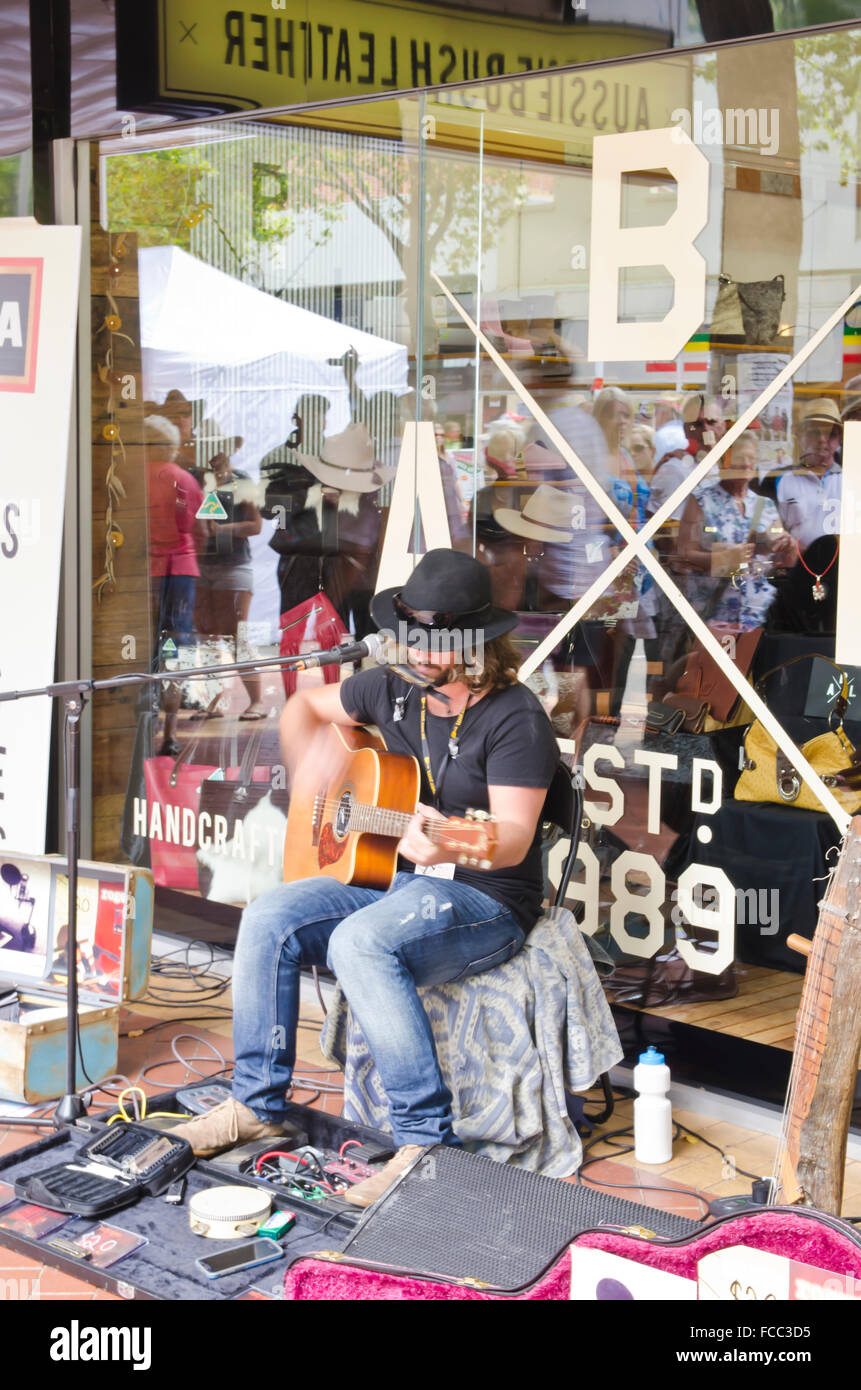 Músico callejero cantando y tocando la guitarra en Tamworth País Music Festival 2016 con espectadores reflejado en el escaparate. Foto de stock