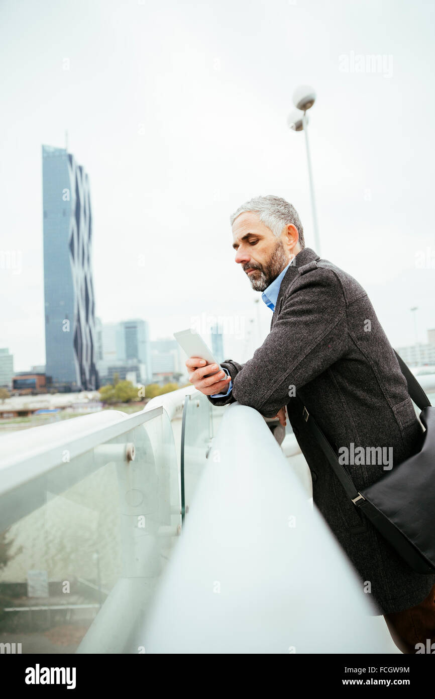 El Austria de Viena, empresario de pie sobre Reichsbruecke mirando su smartphone Foto de stock