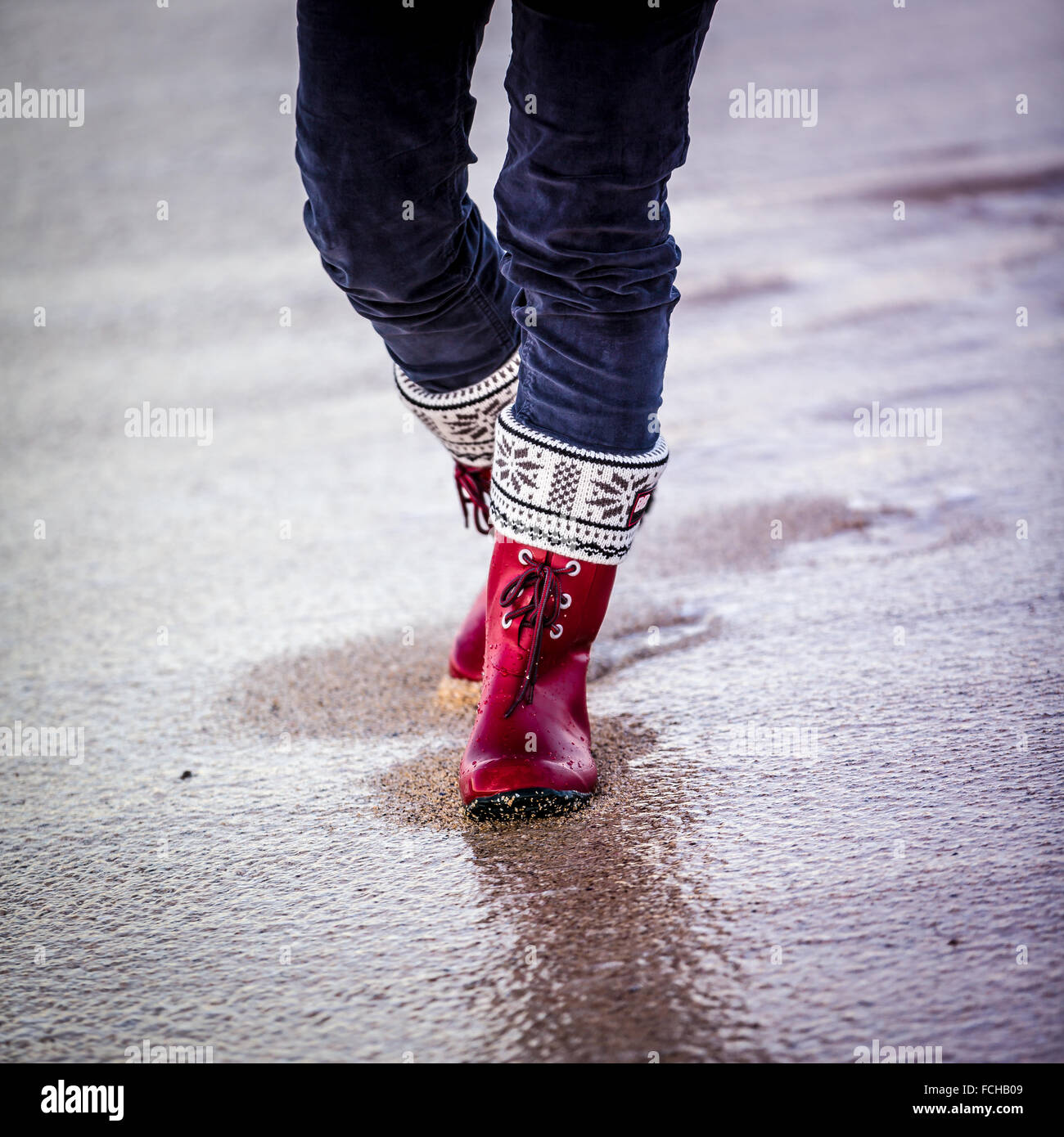 lago Equipo salario Mujer con botas rojas y pantalones de terciopelo azul camina en una playa  húmeda Fotografía de stock - Alamy