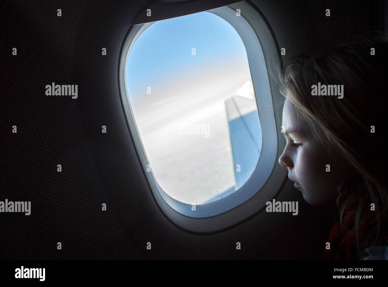 Niña mirando por la ventana del avión mientras avión está volando. Foto de stock