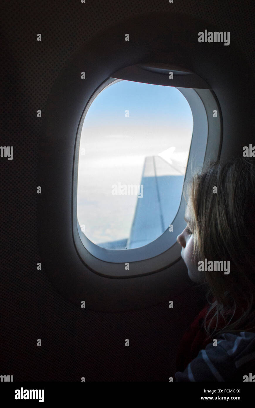 Niña mirando por la ventana del avión mientras avión está volando. Foto de stock
