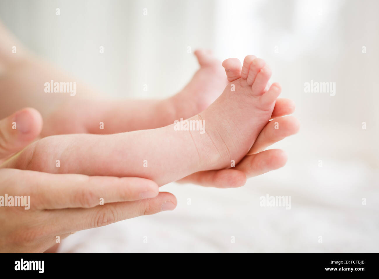 Las manos de la madre sosteniendo las piernas del bebé en studio Foto de stock