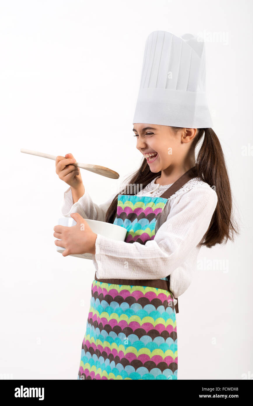Linda niña vestida como un chef en un toque colorido delantal blanco y divierten riendo Foto de stock