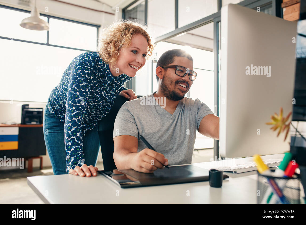 Dos jóvenes diseñadores masculinos y femeninos trabajando juntos, con el hombre edición de ilustraciones utilizando tableta gráfica y un lápiz. Creative púb Foto de stock