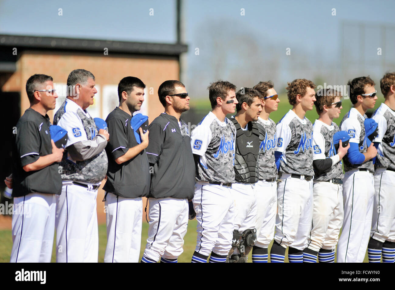 Los jugadores y entrenadores del equipo de béisbol de una escuela secundaria línea durante el himno nacional previo al inicio del juego. Ee.Uu.. Foto de stock
