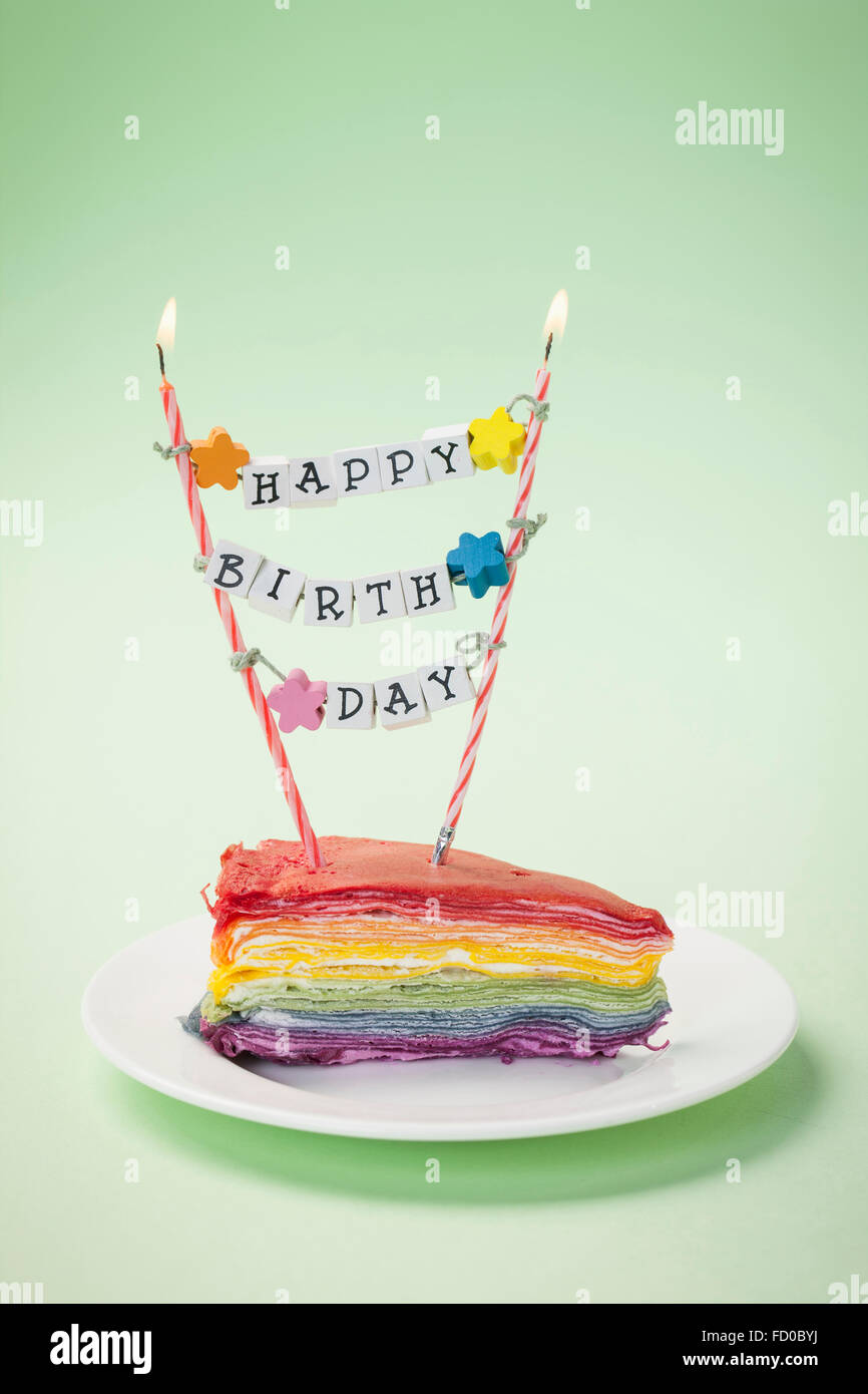 Colorido pedazo de pastel en un plato con las velas y el mensaje de Feliz cumpleaños Foto de stock