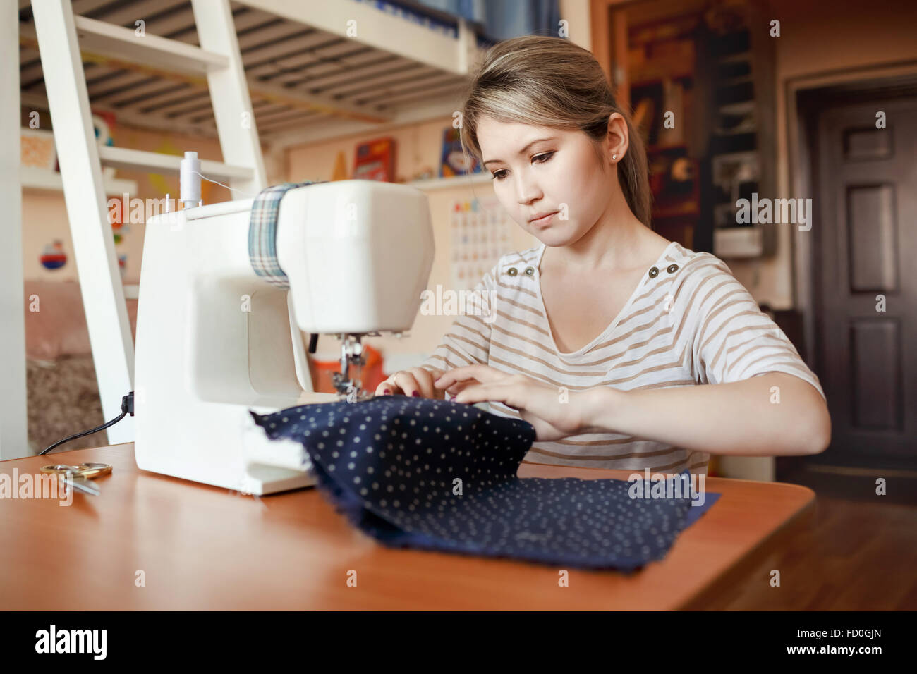 Mujer joven coser con máquina de coser en casa mientras está sentado en su  lugar de trabajo. Diseñador de moda cuidadosamente creando nuevos estilos  de moda. Modista hace ropa adicional a través