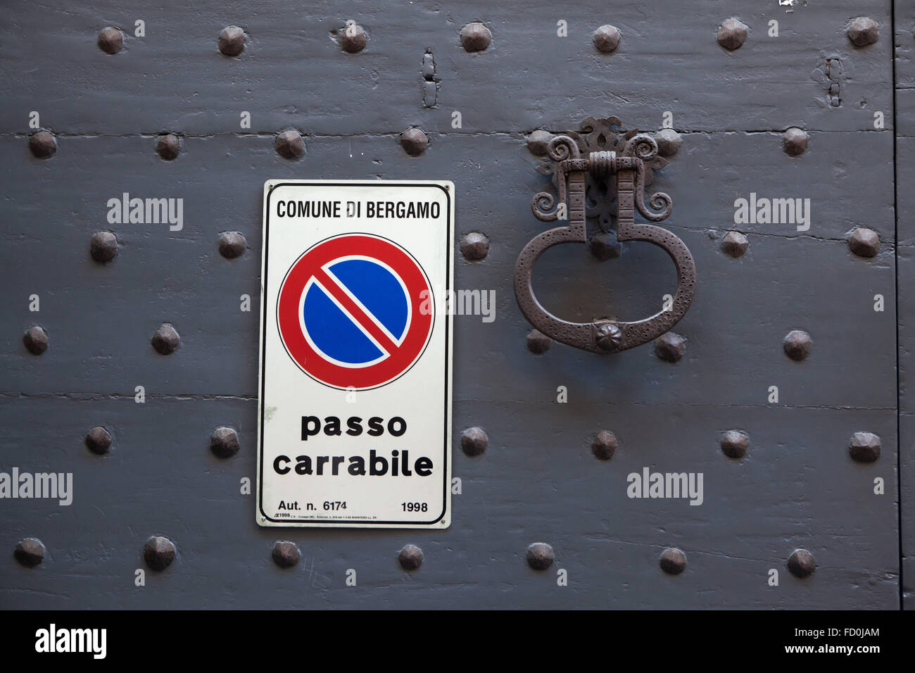 Metal viejo doorknocker y ninguna señal de estacionamiento en la puerta de madera pintada de negro con remaches fijos en Bérgamo, Lombardía, Italia. Foto de stock