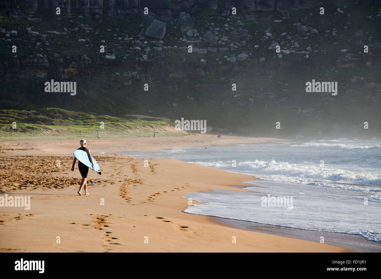 El ciclista de la tabla de surf camina por el extremo norte de la playa en Palm Beach de Sydney en Nueva Gales del Sur, Australia a primera hora de la mañana Foto de stock