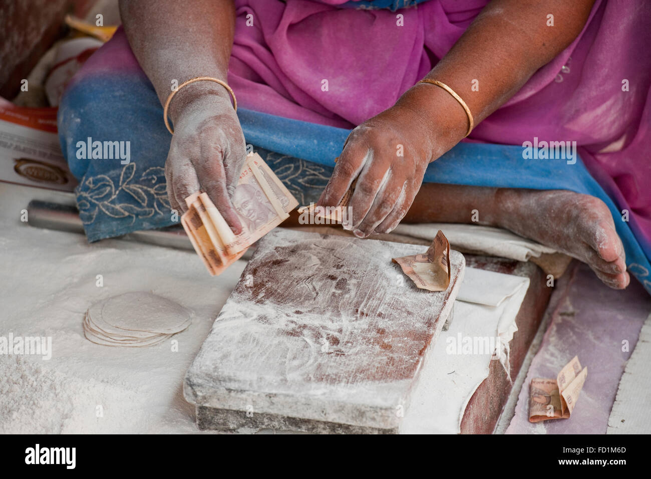 Una imagen de un chappati creadores de manos y brazos cubiertos de harina y contando rupias indias por encima de un bloque de picado de madera Foto de stock