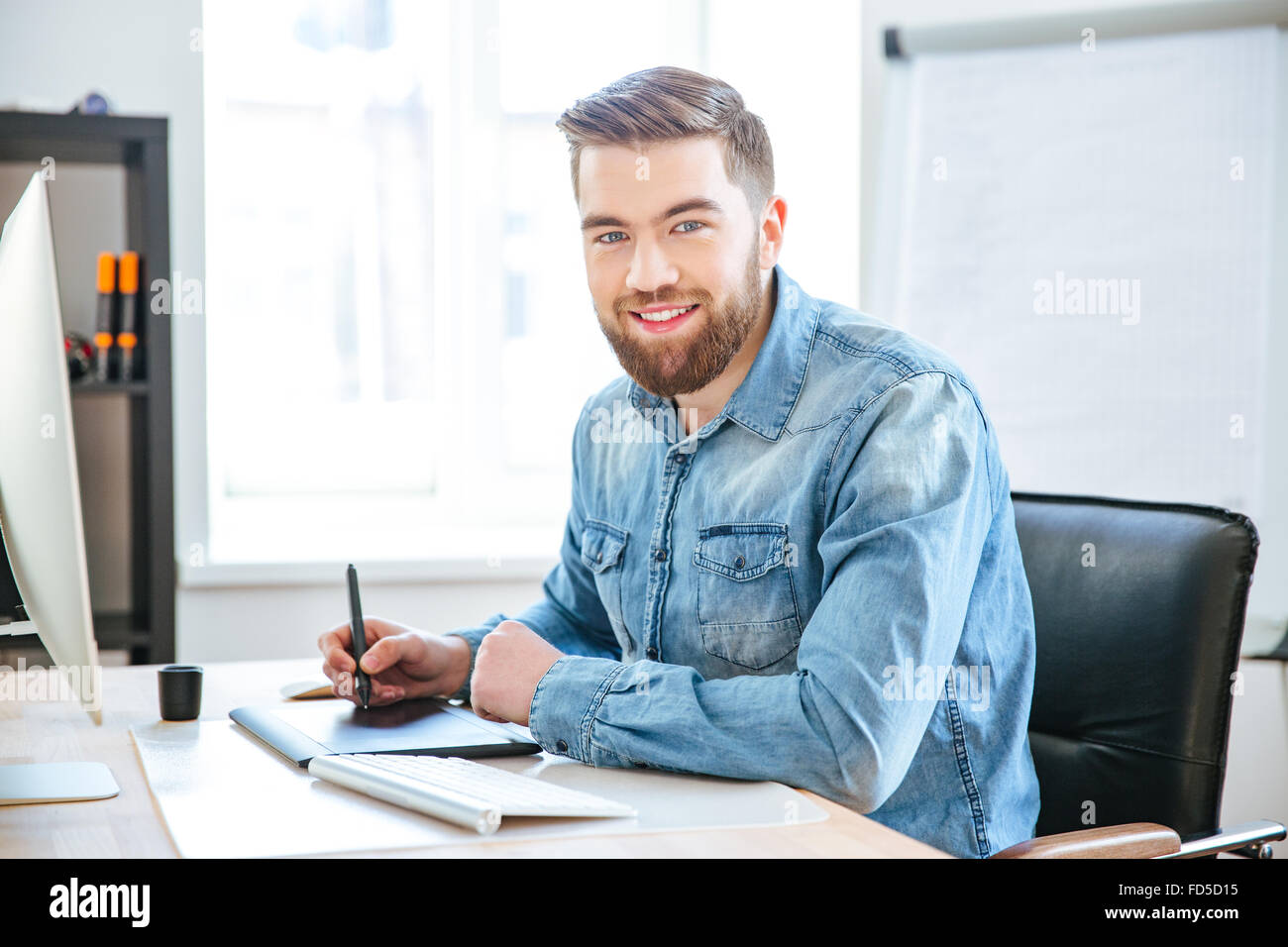 Retrato de feliz atractivo diseñador joven en jeans shirt trabaja con pen tablet con lápiz en Office Foto de stock