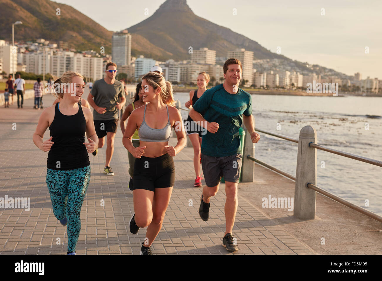 Los jóvenes que corre a lo largo de un paseo marítimo. Colocar los jóvenes corredores formación al aire libre junto a la playa, con dos mujeres atletas cha Foto de stock