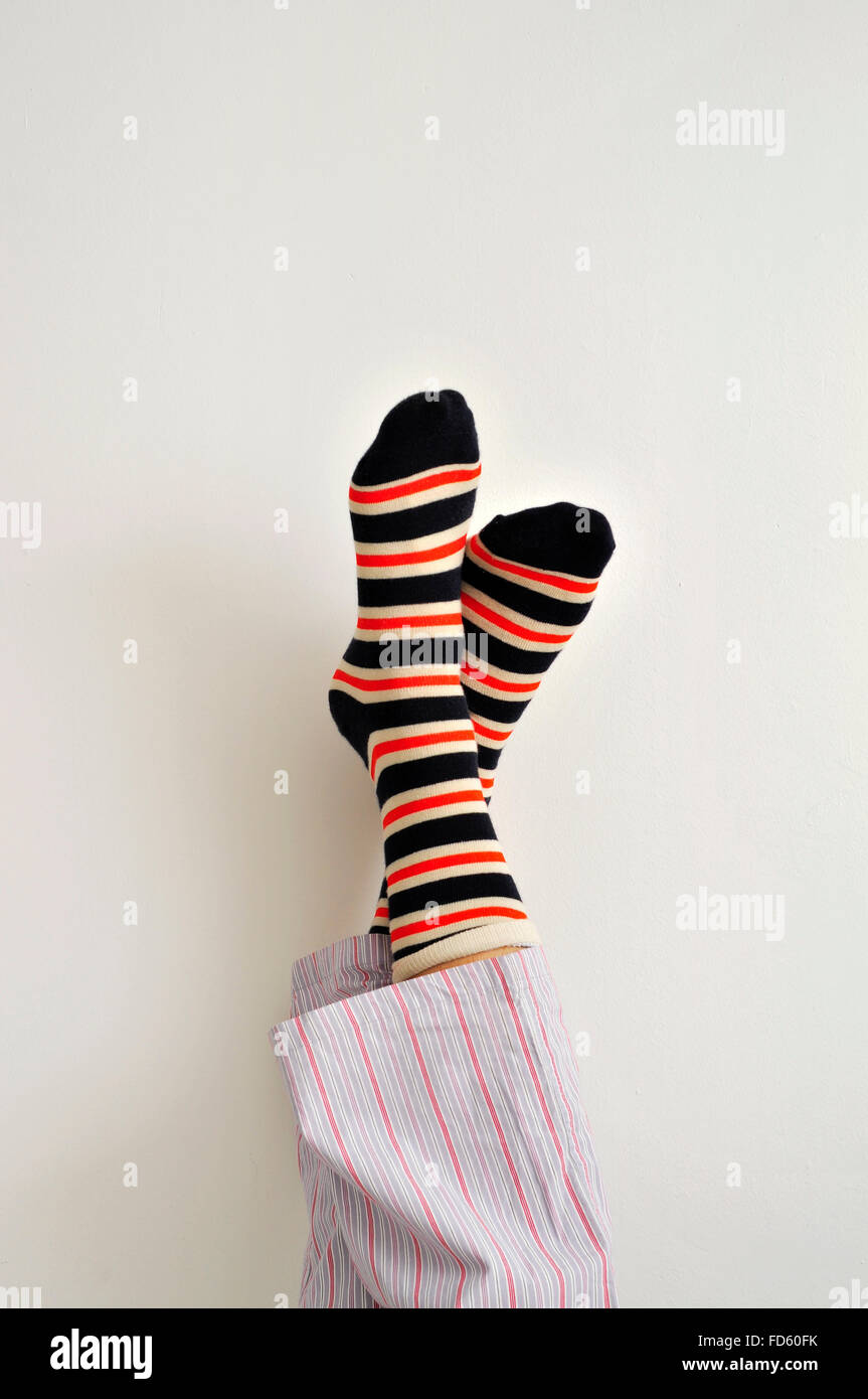 Primer plano de un joven en pijama vistiendo coloridos calcetines de rayas con sus pies contra la pared Foto de stock