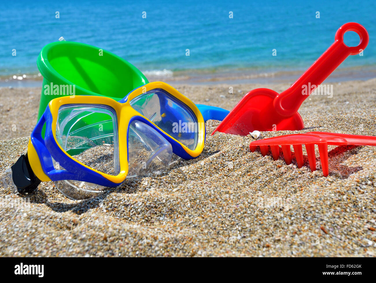 Juguetes para bebé en la arena de la playa frente al mar azul Foto de stock