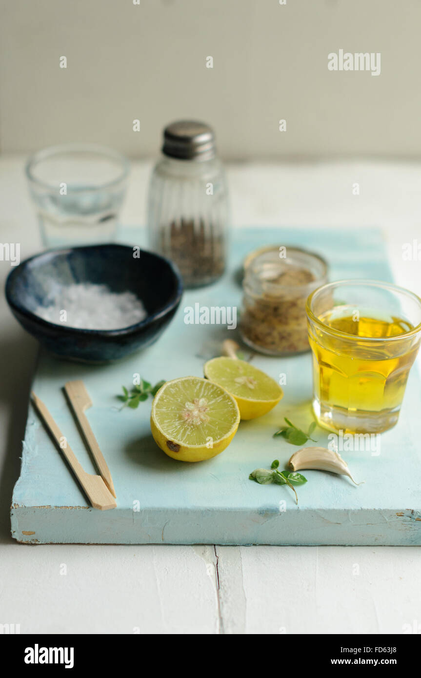 Ingredientes para el aderezo de ensalada sobre un fondo blanco y azul con limón, aceite de oliva, sal de mar, la mostaza, la pimienta y el ajo Foto de stock