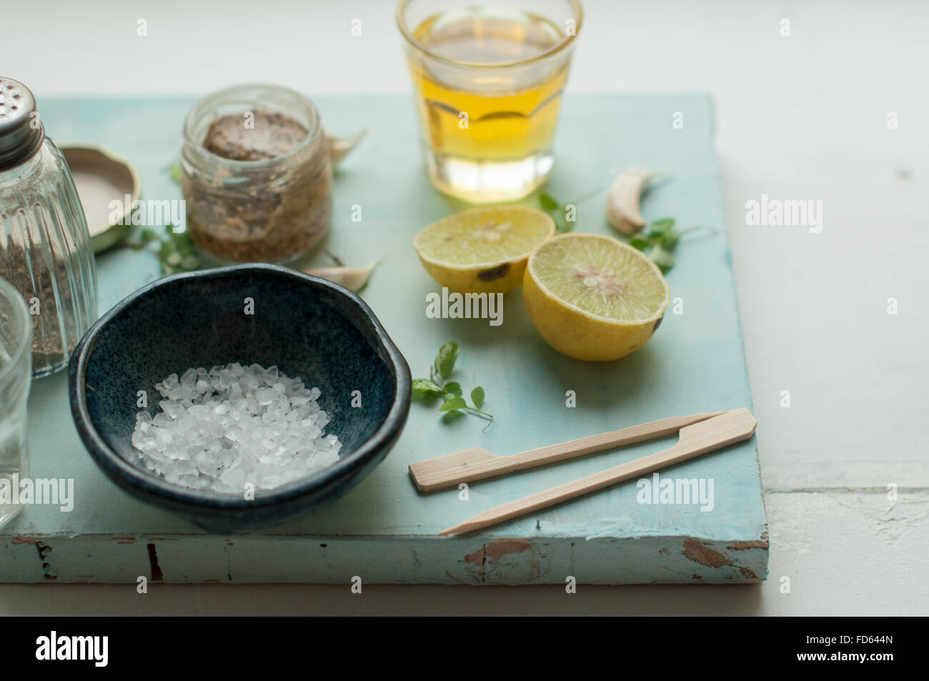 Ingredientes para el aderezo de ensalada sobre un fondo blanco y azul con limón, aceite de oliva, sal de mar, la mostaza, la pimienta y el ajo Foto de stock
