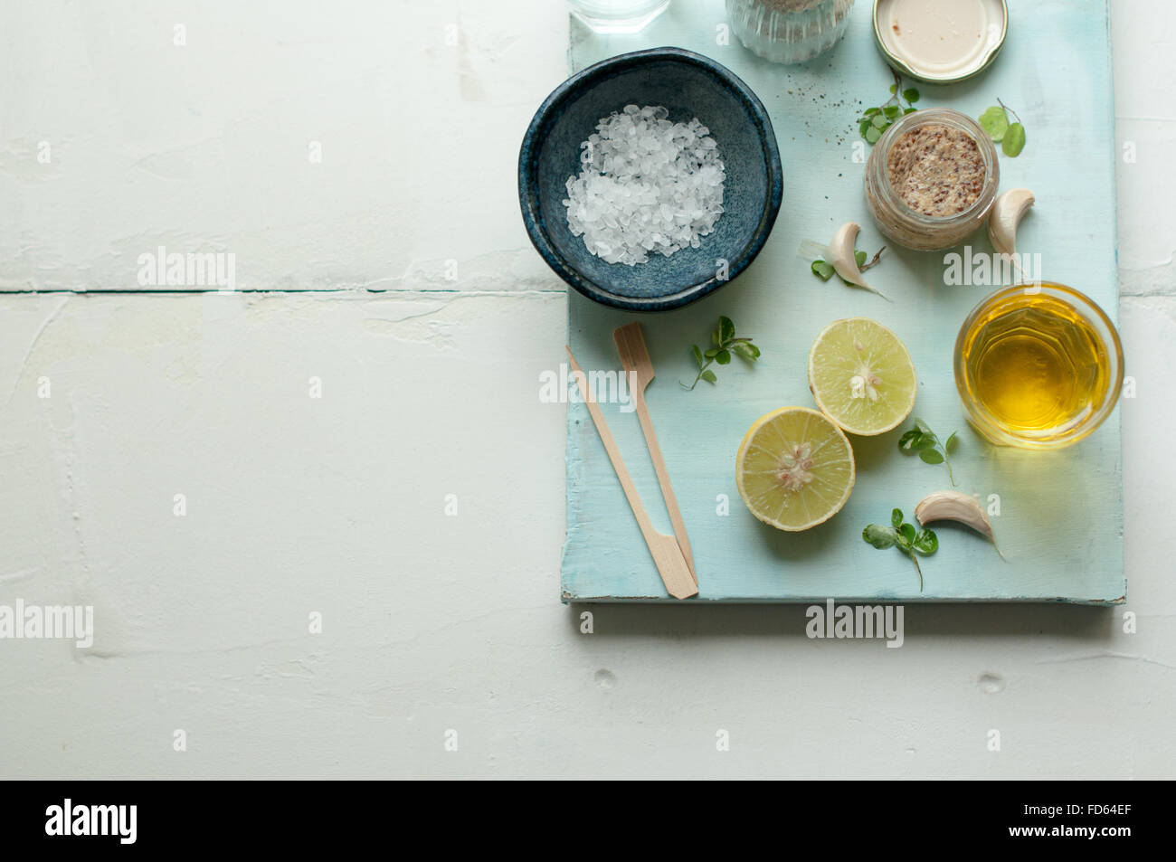 Ingredientes para el aderezo de ensalada sobre un fondo blanco y azul con limón, aceite de oliva, sal de mar, la mostaza, la pimienta y el ajo Foto de stock