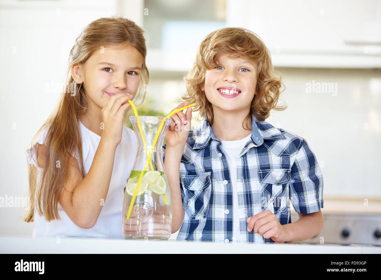 Niño y niña bebe agua de limón fresco con paja en la cocina Foto de stock