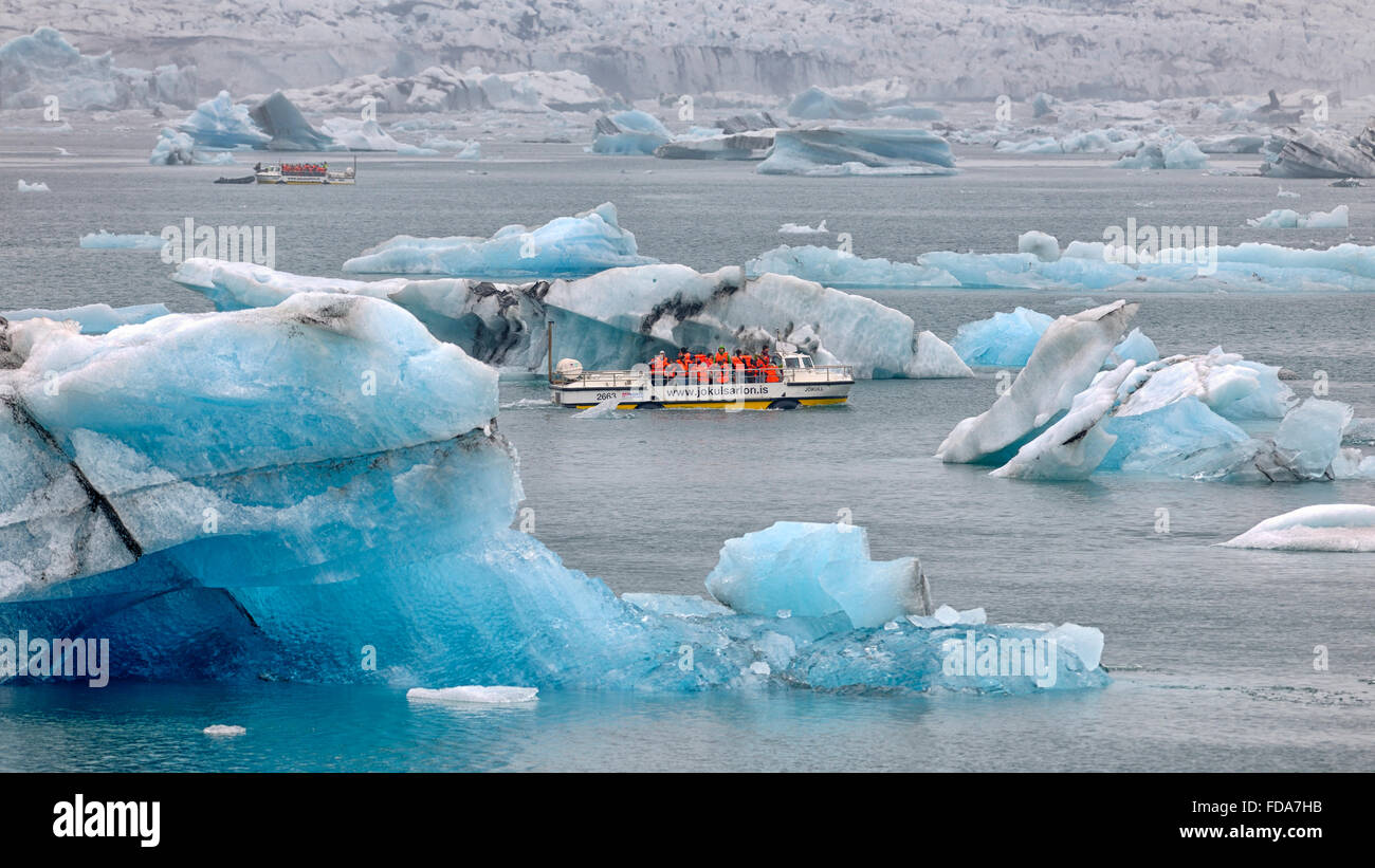 Flotan icebergs azules en la laguna glaciar Jökulsárlón con barcos turísticos, detrás del glaciar de Vatnajökull, región sur Foto de stock