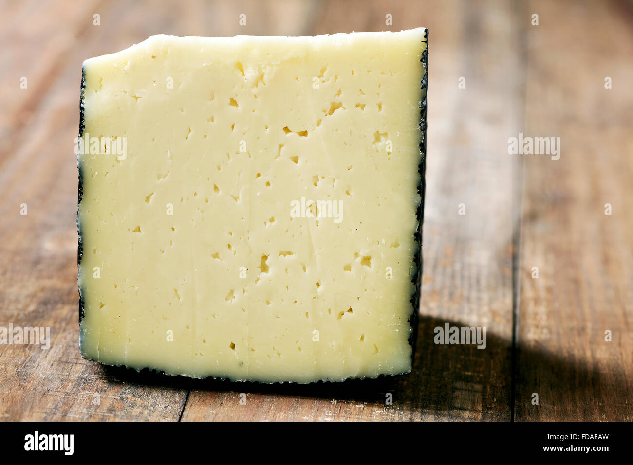 Primer plano de un trozo de queso manchego de España sobre una tabla de madera rústica Foto de stock