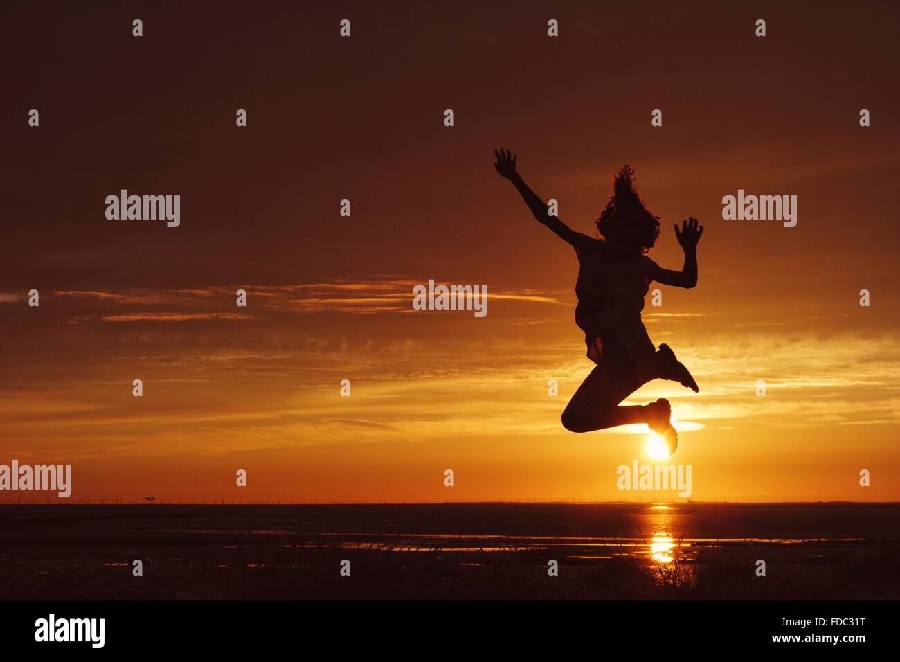 Joven Saltando delante de la puesta de sol en Heysham en Morecambe Bay Foto de stock