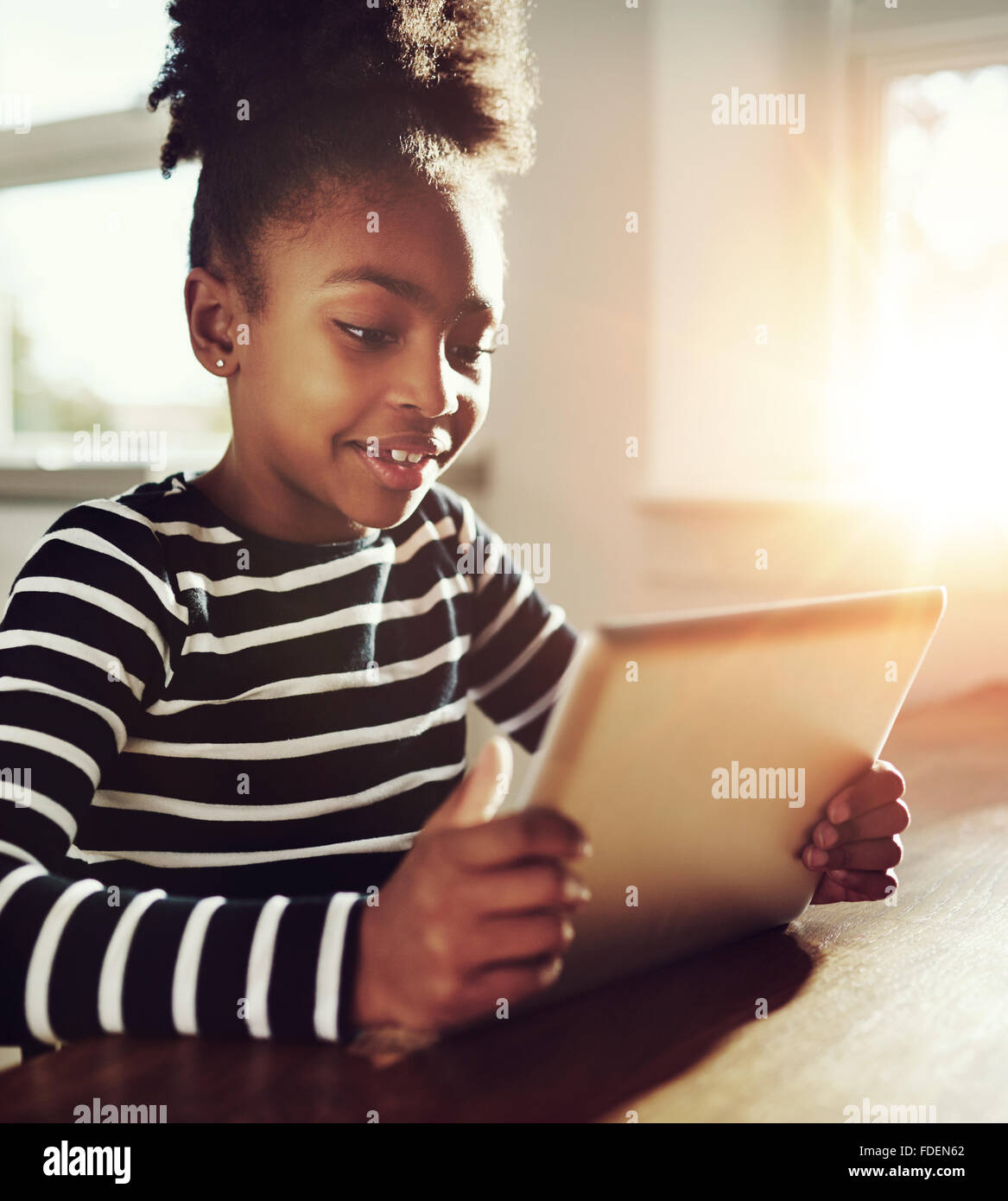 Cerrar bastante negro niña jugando juegos en línea en su Tablet PC con feliz expresión facial. Foto de stock