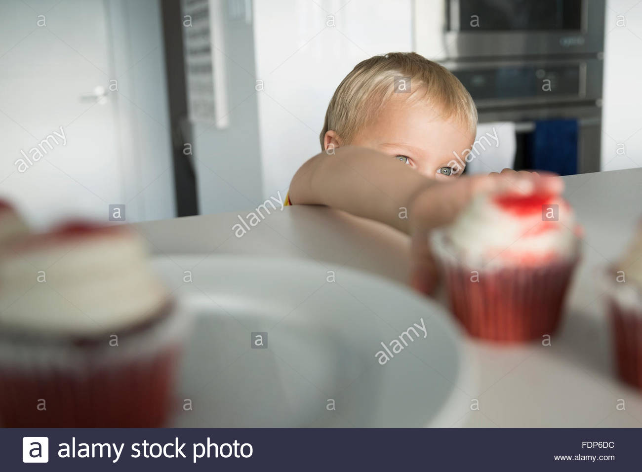 Boy alcanzando cupcake en cocina Foto de stock