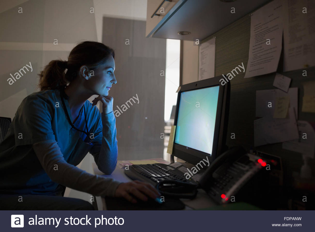 Enfermera que trabaja en un portátil en la estación de enfermeras oscuro Foto de stock