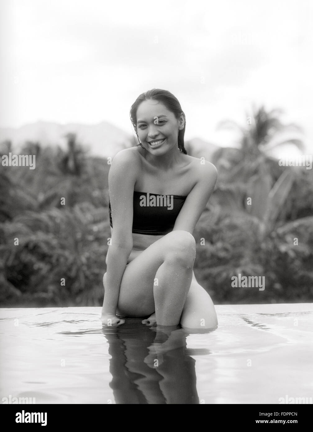 Una mujer se sienta en la cornisa de la piscina infinity en la Granja de San Benito, Filipinas. Foto de stock